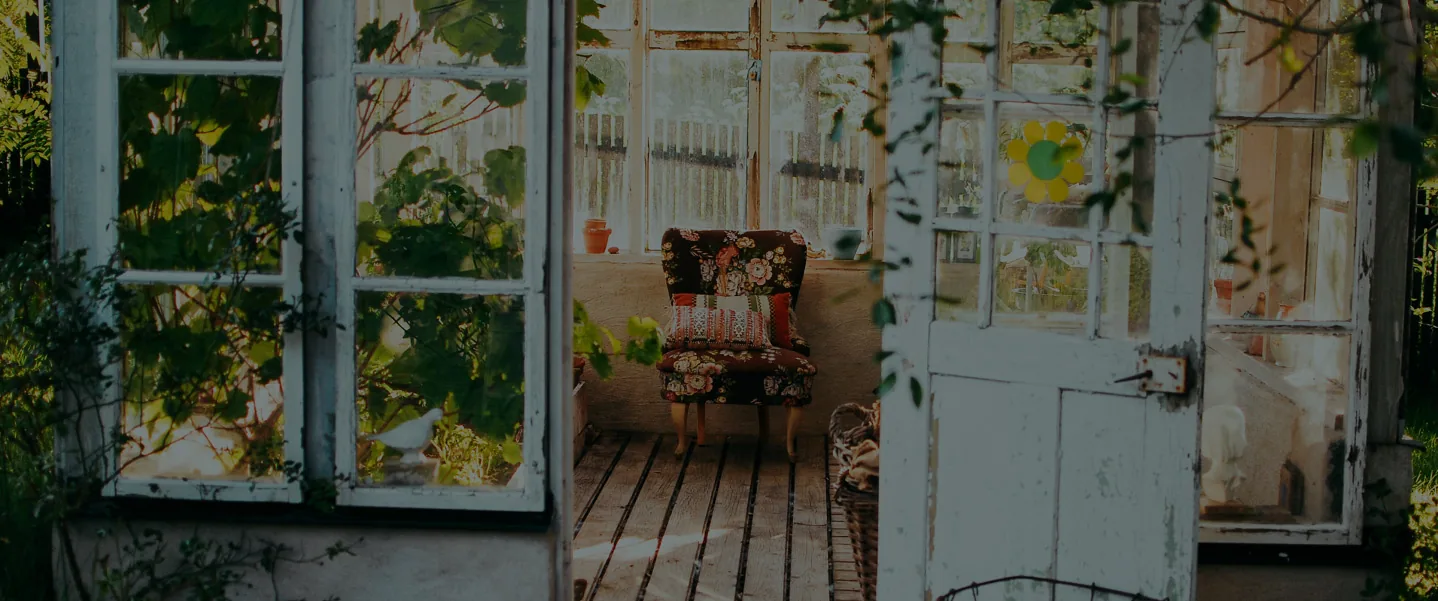 A sunlit garden room with an armchair, seen through open cottage doors